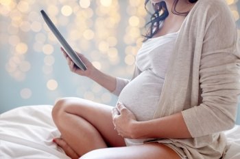 pregnancy, technology, people and expectation concept - close up of pregnant woman with tablet pc computer in bed over holidays lights background