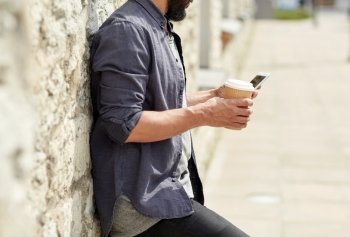 leisure, technology, communication and people concept - close up of man with smartphone drinking coffee from disposable paper cup on city street