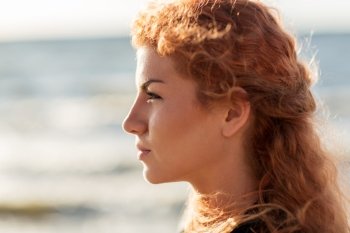 people, facial expression and emotion concept - happy young redhead woman face on beach