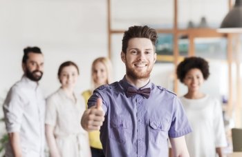 business, startup, people, gesture and teamwork concept - happy young man with beard and bow tie showing thumbs up over creative team in office
