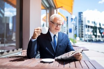 business, mass media, news and people concept - senior businessman reading newspaper and drinking coffee at city street cafe. senior businessman with newspaper drinking coffee
