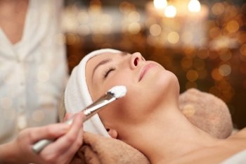 people, beauty, spa, cosmetology and skincare concept - close up of beautiful young woman lying with closed eyes and cosmetologist applying facial mask by brush in spa