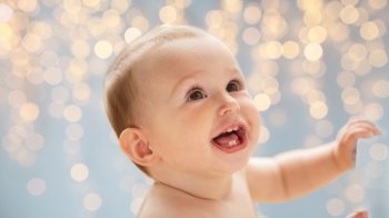childhood, babyhood, emotions and people concept - happy little baby boy or girl looking up over holidays lights background