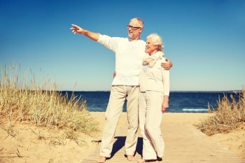 family, age, travel, tourism and people concept - happy senior couple pointing finger to something on summer beach