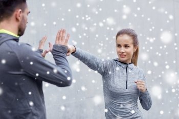 fitness, sport, martial arts, self-defense and people concept - happy woman with personal trainer working out strike outdoors over snow