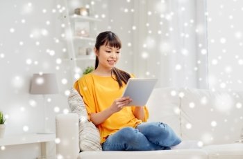 people, technology and leisure concept - happy young asian woman sitting on sofa with tablet pc computer at home over snow