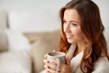 leisure, drink, winter and people concept - happy young woman with cup of coffee or cocoa at home