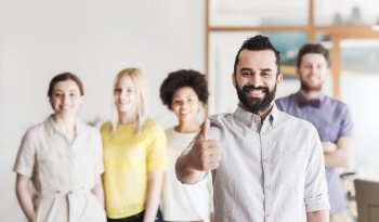 business, startup, people, gesture and teamwork concept - happy young man with beard showing thumbs up over creative team in office