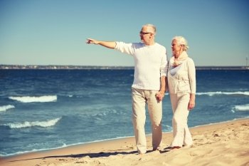 family, age, travel, tourism and people concept - happy senior couple walking and pointing finger to something on summer beach