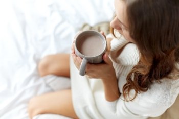 morning, coziness, winter and people concept - close up of young woman with cup of coffee or cacao in bed at home