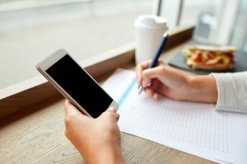 business, people, technology and lifestyle concept - woman with smartphone and paper form writing at cafe
