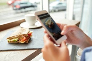 food, culinary, technology and people concept - woman hands with smartphone photographing panini sandwich at restaurant