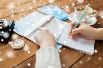winter holidays, tourism, travel, destination and people concept - traveler hands with map and coffee writing to notebook over snow