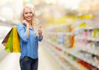 retail, people, gesture and sale concept - smiling woman with many shopping bags showing thumbs up over supermarket background