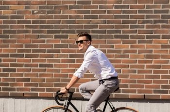 lifestyle, transport and people concept - young man in sunglasses riding bicycle on city street over brickwall