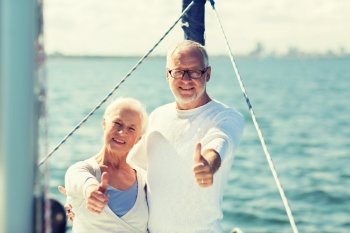 sailing, age, tourism, travel and people concept - happy senior couple hugging on sail boat or yacht deck floating and showing thumbs up in sea