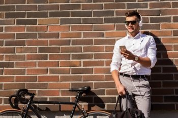 people, technology and lifestyle - happy young man with headphones, smartphone and bicycle listening to music in city
