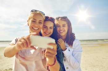summer vacation, holidays, travel, technology and people concept- group of smiling young women taking sulfide with smartphone on beach