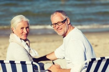 family, age, travel, tourism and people concept - happy senior couple sitting on deck chairs on summer beach