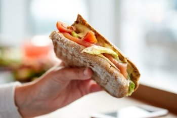 food, dinner, eating and people concept - hand with salmon panini sandwich with tomatoes and cheese at restaurant
