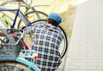 people, security, safety and transport - man fastening bicycle lock on street parking