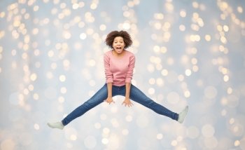 people, motion and action concept - happy african american young woman jumping over holidays lights background