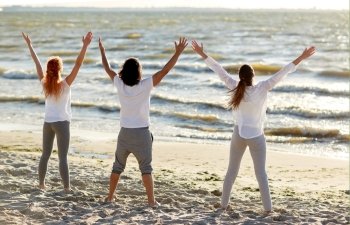 fitness, sport, yoga and healthy lifestyle concept - group of people meditating on beach