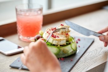food, culinary, haute cuisine and people concept - woman eating goat cheese salad with vegetables and dried raspberries using fork and knife at restaurant or cafe