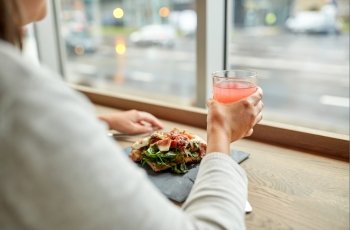 food, drink, eating and people concept - woman with glass of juice and prosciutto ham salad on stone plate at restaurant