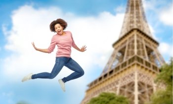 people, motion and action concept - happy african american young woman jumping over paris eiffel tower background