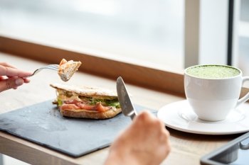 food, dinner and people concept - woman eating salmon panini sandwich with cup of matcha green tea latte at restaurant