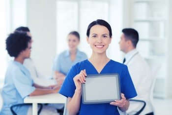 clinic, profession, people and medicine concept - happy female doctor or nurse showing tablet pc computer blank screen over group of medics meeting at hospital