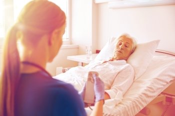 medicine, age, support, health care and people concept - doctor or nurse adjusting bed with remote control for senior woman patient at hospital ward