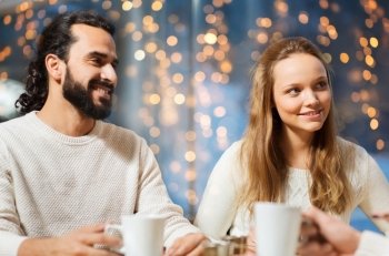people, leisure and communication concept - happy friends or couple meeting and drinking tea or coffee at cafe over holidays lights background