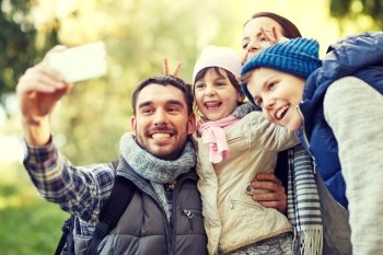 travel, tourism, hike, technology and people concept - happy family with backpacks taking selfie by smartphone outdoors