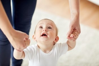 family, child, childhood and parenthood concept - close up of happy little baby learning to walk with mother help at home