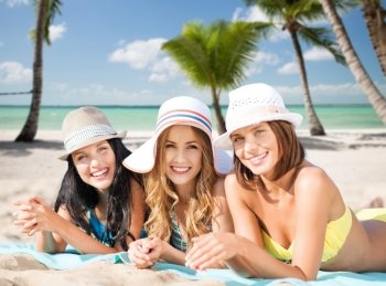 summer holidays, travel, people and vacation concept - happy young women in bikinis sunbathing over exotic tropical beach with palm trees and sea shore background