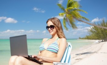 summer holidays, vacation, travel, technology and people concept - smiling women in sunglasses with laptop computer sunbathing in lounge over exotic tropical beach with palm tree background