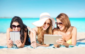 summer holidays, technology, people, travel and internet concept - happy young women in bikinis with tablet pc computers sunbathing over exotic tropical beach and sea shore background