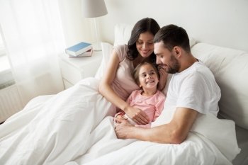 people, family and morning concept - happy child with parents in bed at home