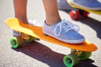 skateboarding, leisure, extreme sport and people concept - close up of young woman legs riding short modern cruiser skateboard on road