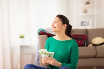 vacation, tourism, travel, finances and people concept - happy young woman with money and bag at home
