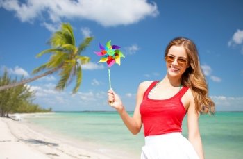 summer holidays, travel, people and vacation concept - happy young woman in sunglasses with pinwheel over exotic tropical beach with palm trees and sea shore background