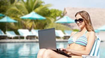 summer holidays, vacation, technology, people and internet - happy young woman in shades with laptop computer over exotic beach with palm trees and pool background