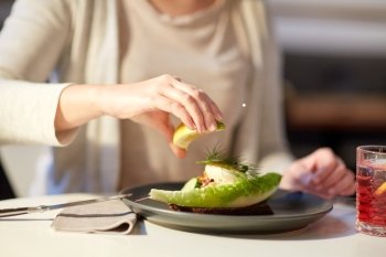 food, new nordic cuisine and people concept - woman eating toast skagen with shrimps, lemon mayonnaise, caviar and buttery bread and squeezing lemon at cafe or restaurant
