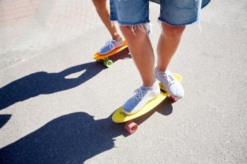 summer, extreme sport and people concept - teenage couple riding short modern cruiser skateboards on city road
