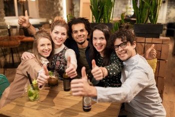 leisure, party, people and holidays concept - happy friends with drinks showing thumbs up at bar or cafe