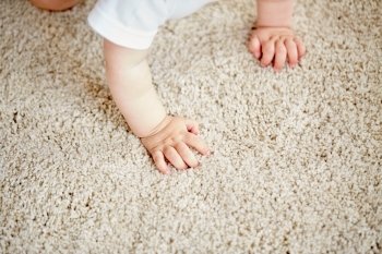 childhood, babyhood and people concept - hands of baby crawling on floor or carpet