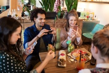 technology, lifestyle and people concept - happy friends with smartphones taking picture of food at restaurant