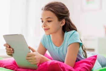 children, technology and communication concept - smiling girl with tablet pc lying in bed at home